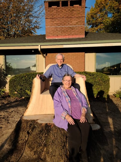 Two seniors enjoying a large wooden chair outdoors