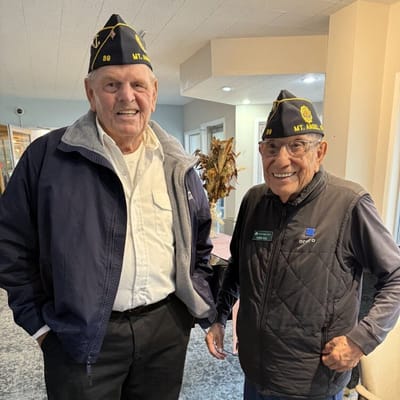 Two smiling residents wearing facility hats in a communal area