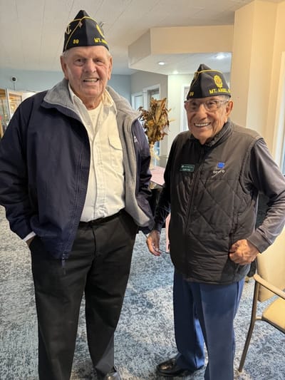 Two smiling residents in veteran hats in a common area
