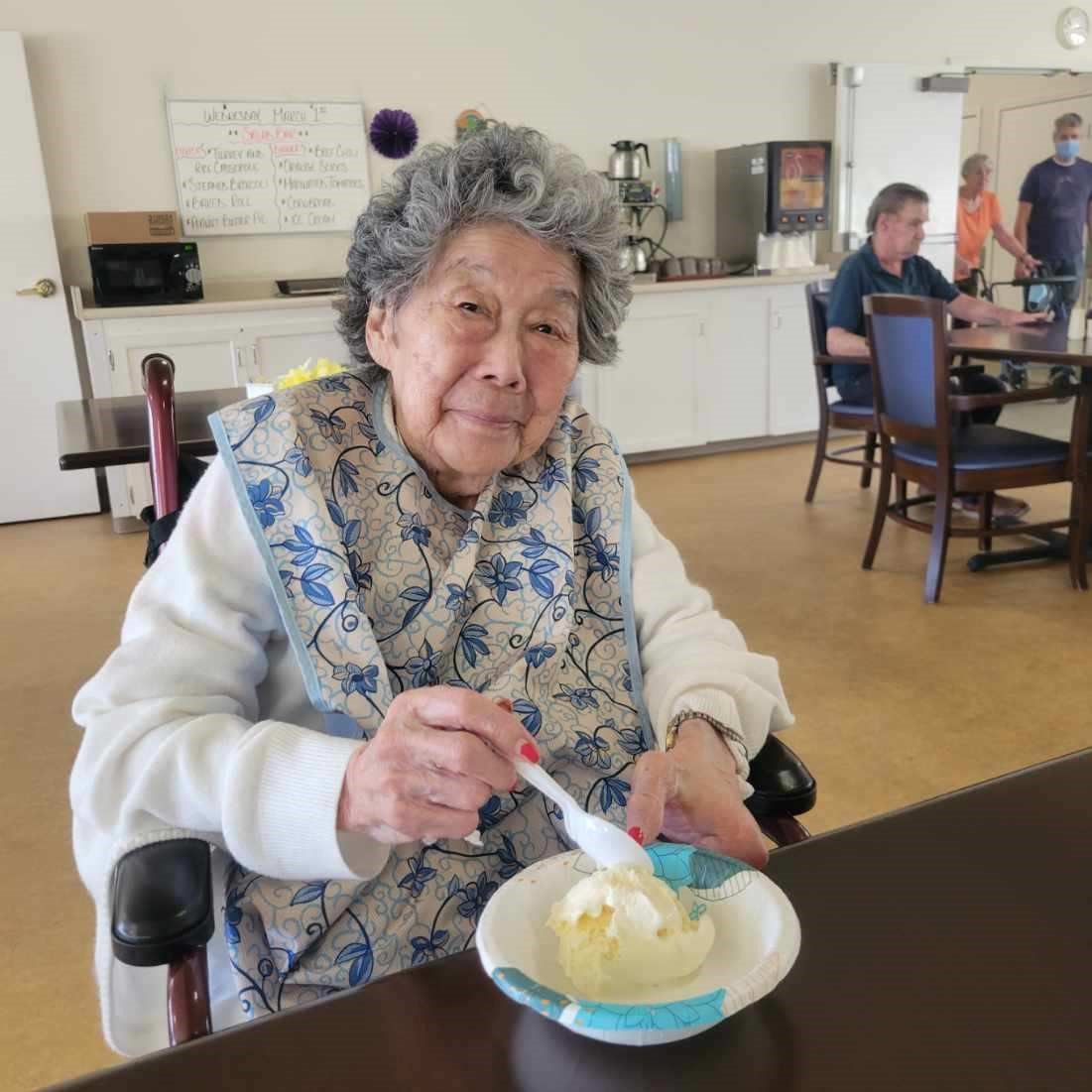 Elderly woman enjoying ice cream in a facility dining area