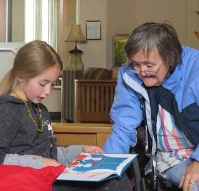 An elderly woman reading with a young girl