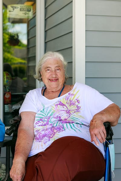 An elderly woman smiling in a wheelchair outside