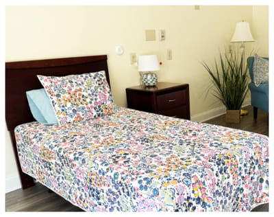 A cozy resident room with a floral bedspread and bedside table