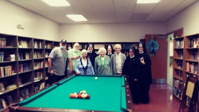 Residents and staff gathered around a pool table in a library.