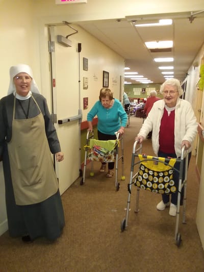 Residents walking in the facility hallway with staff assistance