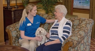 Staff member with resident and a dog in a cozy living area