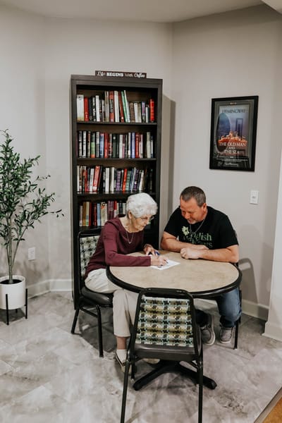 Resident and staff engaging at a table in a cozy reading area
