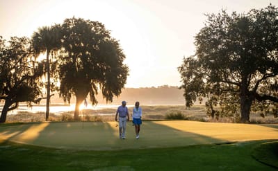 Two people walking on a golf course at sunrise