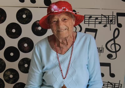 A senior woman smiling, wearing a red hat in front of a musical backdrop