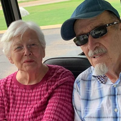 Two seniors smiling in a cart during an outdoor activity