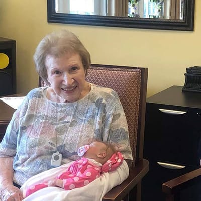 An elderly woman smiling while holding a baby