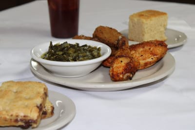 Plate of fried chicken, greens, and cornbread on a table