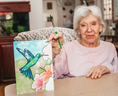 Senior resident painting with a hummingbird illustration
