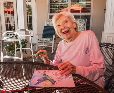 Resident painting at an outdoor table in a vibrant garden