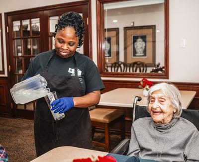 Staff pouring a drink for a smiling resident