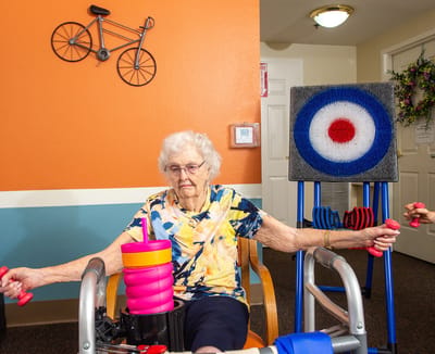 An elderly woman exercising with weights in a colorful activity room
