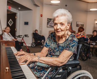 An elderly woman playing piano in a common area