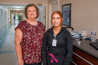 Two staff members posing in a facility corridor