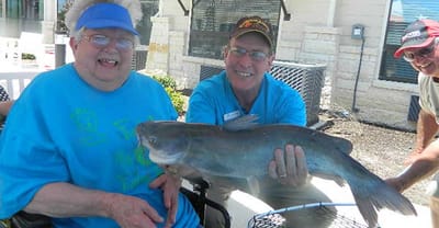 Senior resident smiling, holding a fish with staff member
