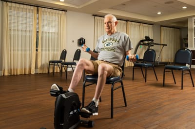 Elderly man exercising with weights in activity room