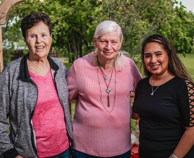 Three women smiling outdoors in a garden area