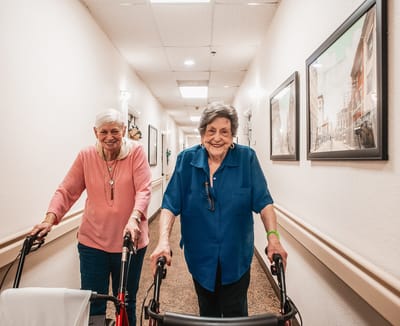 Two residents walking down a hallway with walkers