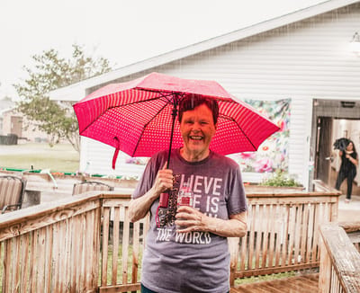 Resident smiling with a red umbrella in the rain