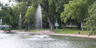 Serene view of a pond with fountains and surrounding greenery