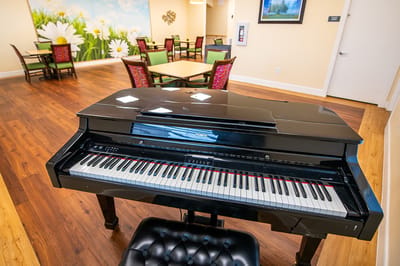 A piano in a common area with tables and chairs