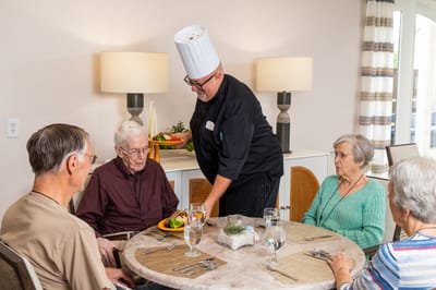 Chef serving food to residents in a dining room