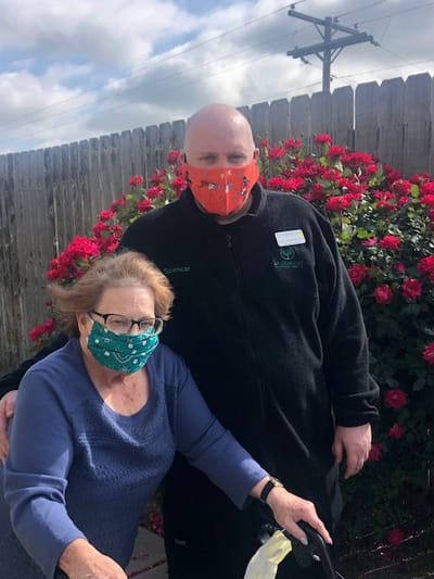 Staff member and resident outdoors in masks near flowers