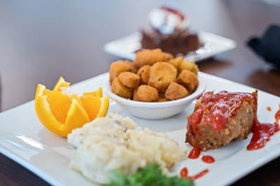 A plate of meatloaf, sides, and orange slice.