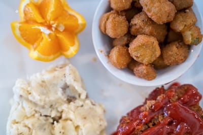 A plate with mashed potatoes, meatloaf, fried okra, and an orange slice.
