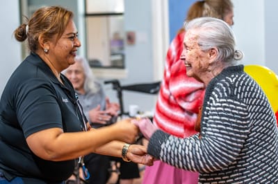 A caregiver dancing with a resident in a bright activity room