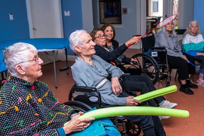 Residents participating in an indoor activity with pool noodles