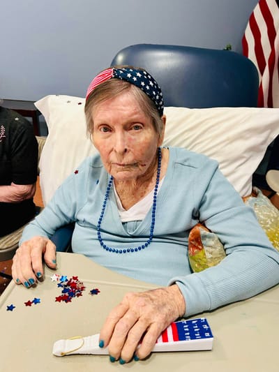 An elderly woman decorates a table with stars and stripes.