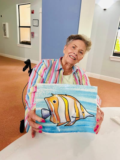 Resident proudly displaying her artwork in a bright room