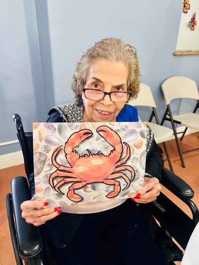 Resident holding up a colorful crab drawing in an activity room