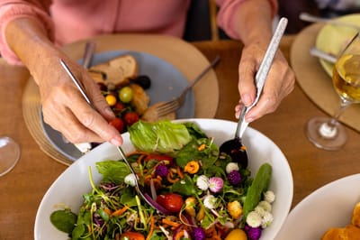 Close-up of hands enjoying a salad at a dining table