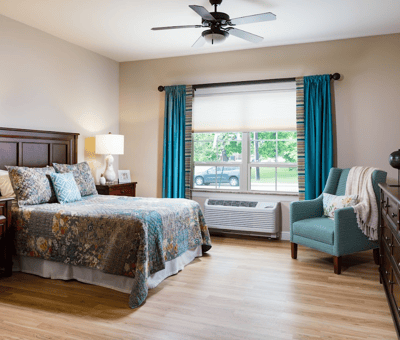 A well-decorated private resident room with a bed and chair