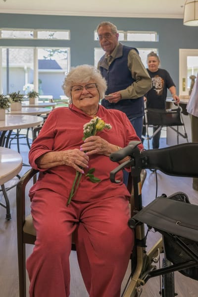 A smiling resident holding flowers in a dining area.