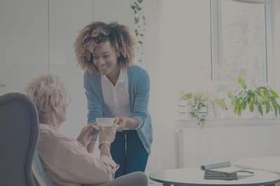 Rocky Mountain Care – Summit Ridge Assisted Living OC LLC, nursing home in Douglas, WY — Caregiver serving tea to a senior resident indoors