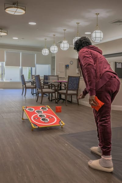 Resident playing a bean bag toss game in a common area