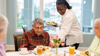 Staff serving a meal to residents in dining area.