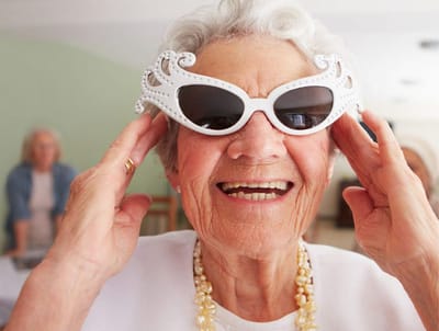 An elderly woman smiling wearing stylish sunglasses inside