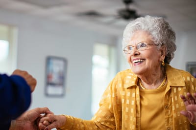 An elderly woman with curly hair smiling while interacting with someone