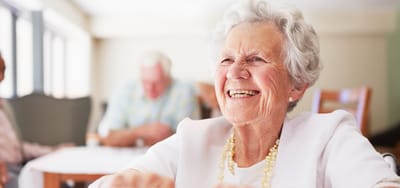 Happy elderly woman smiling in a communal space.