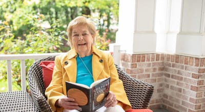 A resident reading on a porch with greenery in the background