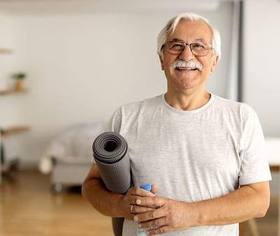 Senior man smiling with yoga mat in a bright room