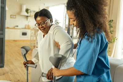 A caregiver assisting a resident with crutches in an interior space